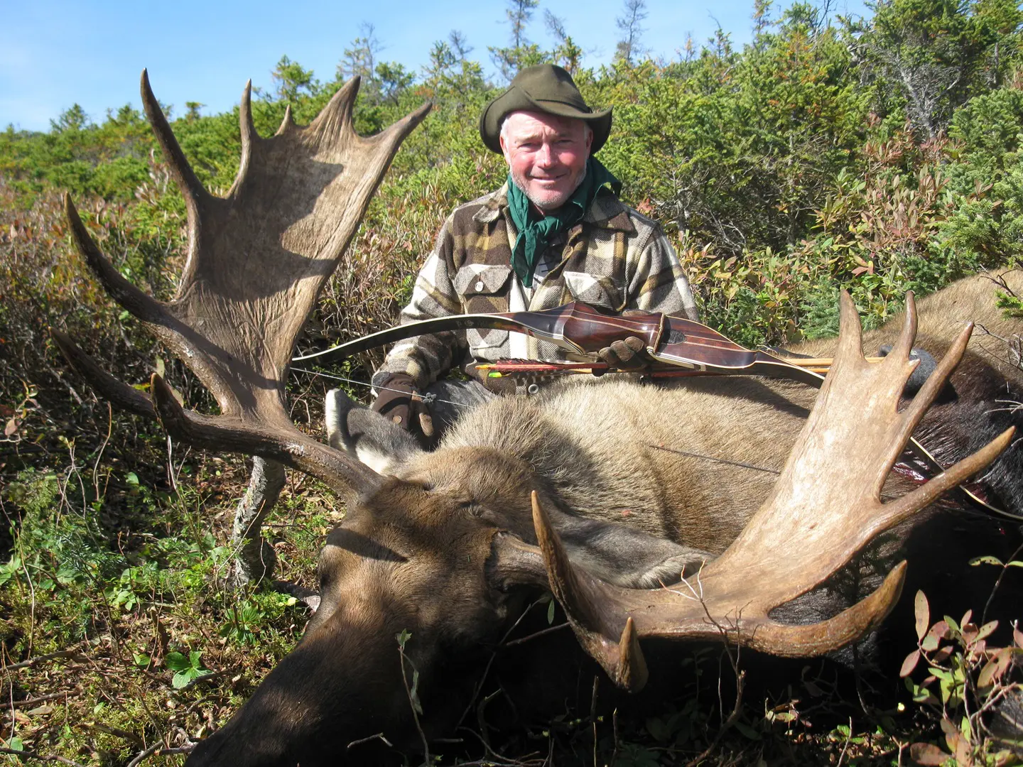 Man holding a bow posing with a hunted moose