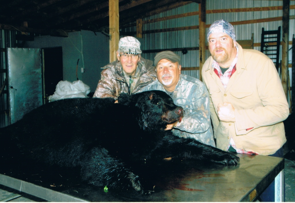 Three men with a black bear on a steel table