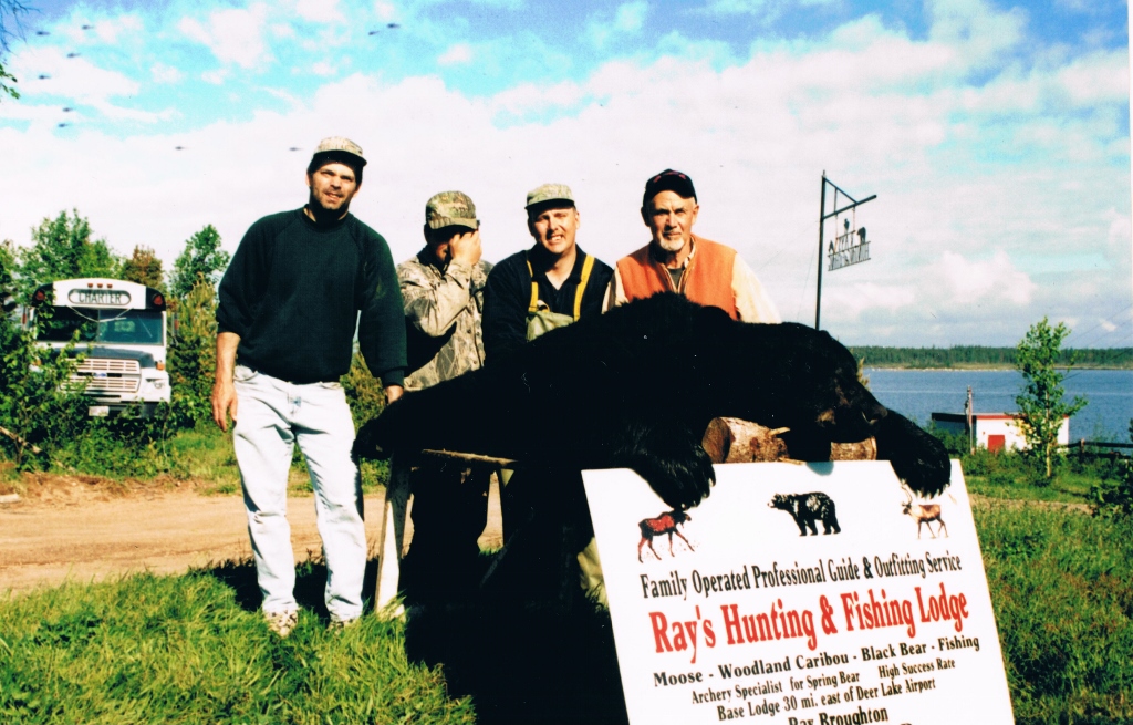 Four men with a hunted black bear at the Ray’s Hunting & Fishing Lodge sign
