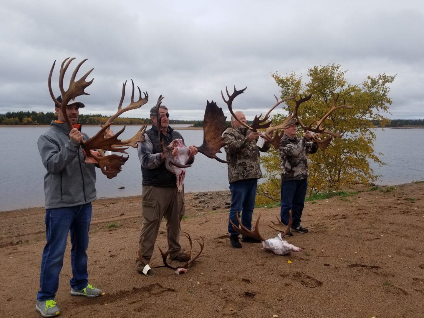 Four men holding antlers in front of a lake